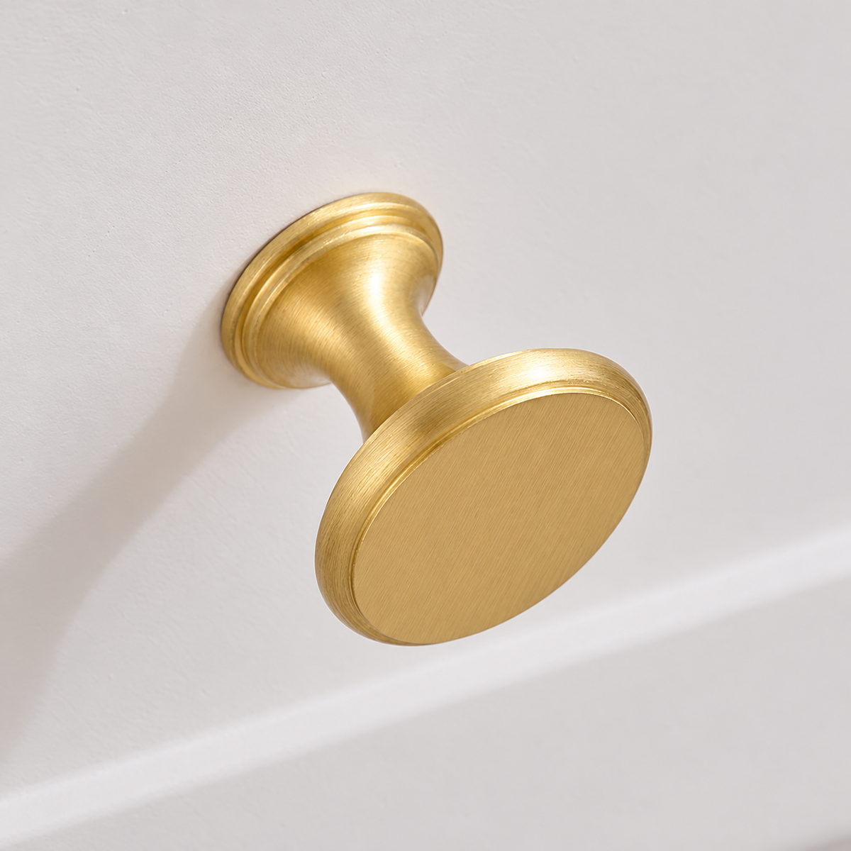 Brushed brass round cabinet knob - installed close-up with visible neck and base